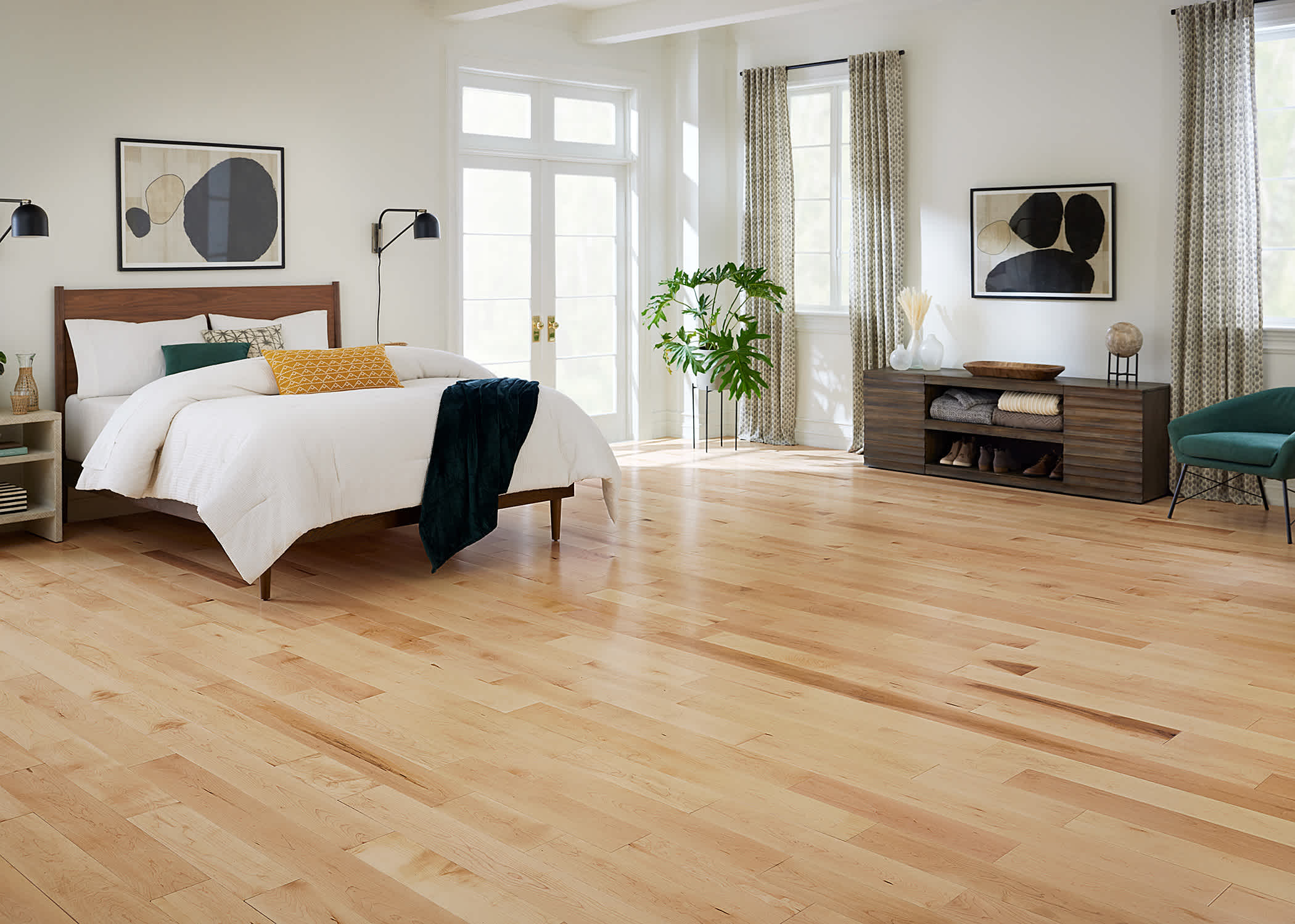 blonde hardwood floor in bedroom with dark brown wood headboard with white bedding plus dark brown low dresser and dark green accent chair