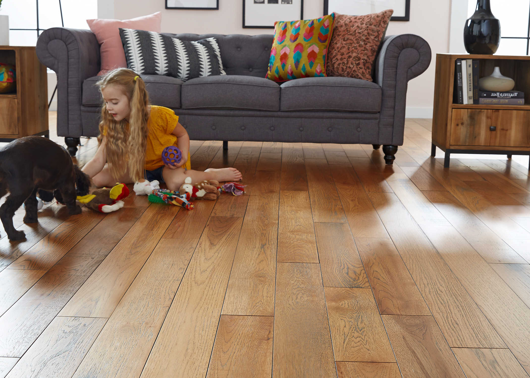 3/4 in. x 5 in. Pepperell Hickory Solid Hardwood Flooring in living room with dark gray sofa and little girl in yellow shirt on floor playing with puppy