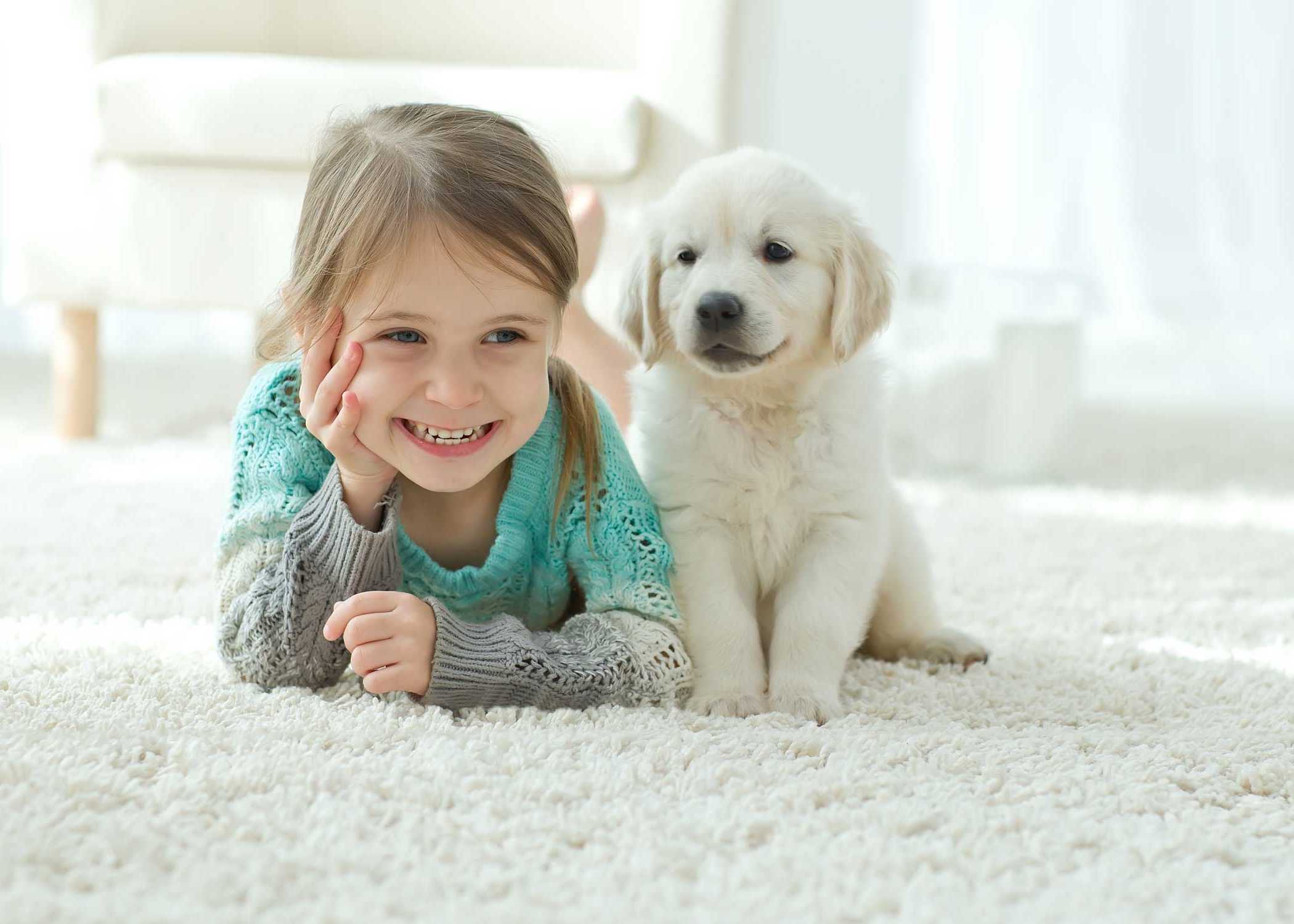 little girl laying next to puppy on white carpeted floor
