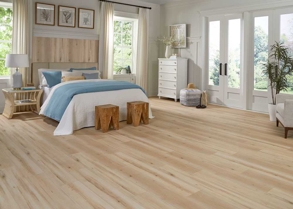 blonde laminate flooring in bedroom with white and blue bedding plus flooring on wall behind upholstered headboard and french doors and white dresser