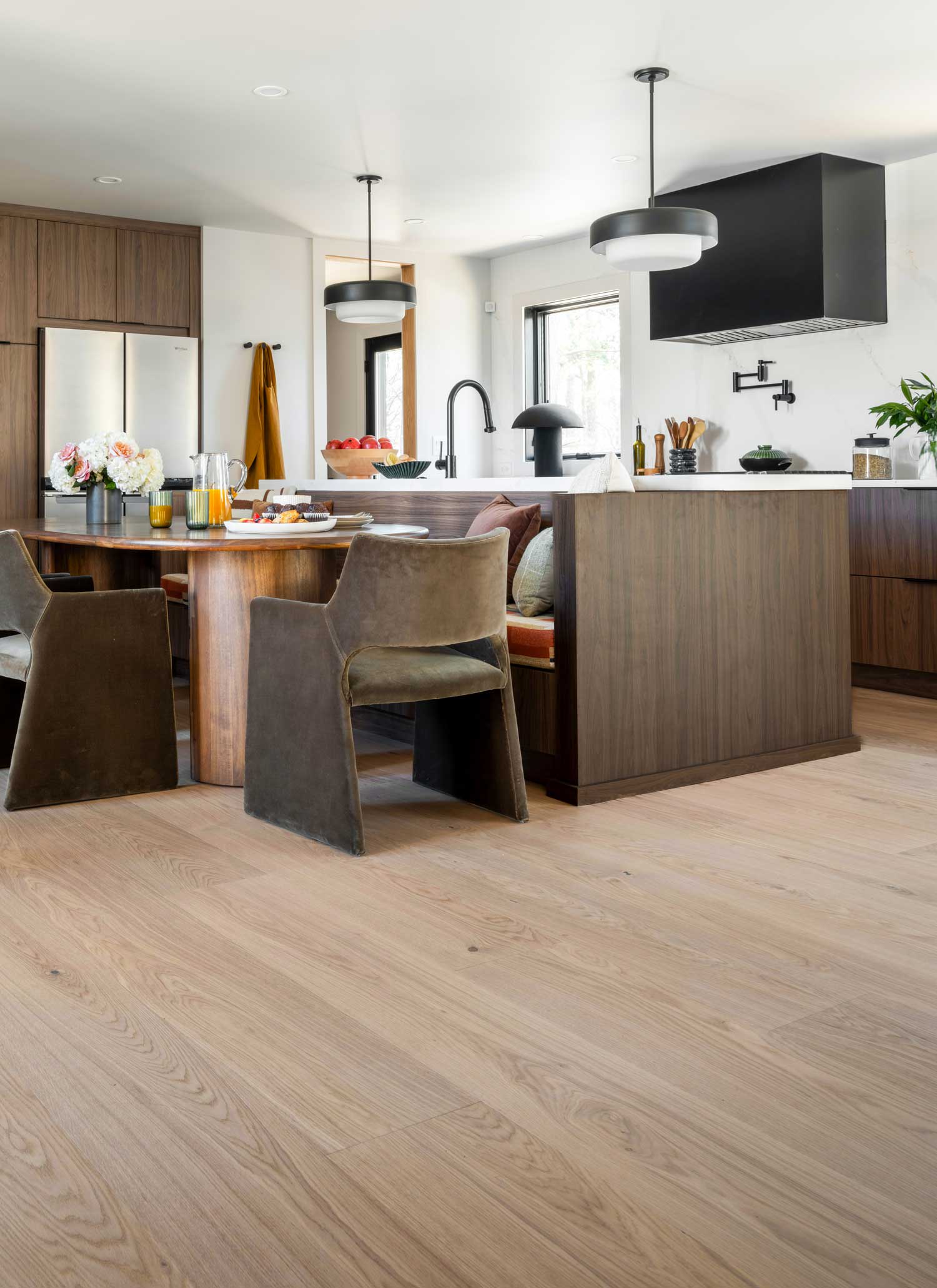 Lagan River White Oak Engineered Hardwood Flooring 2024 HGTV Smart Home kitchen with dark brown cabinetry plus dining area with dark green chairs and bench seating