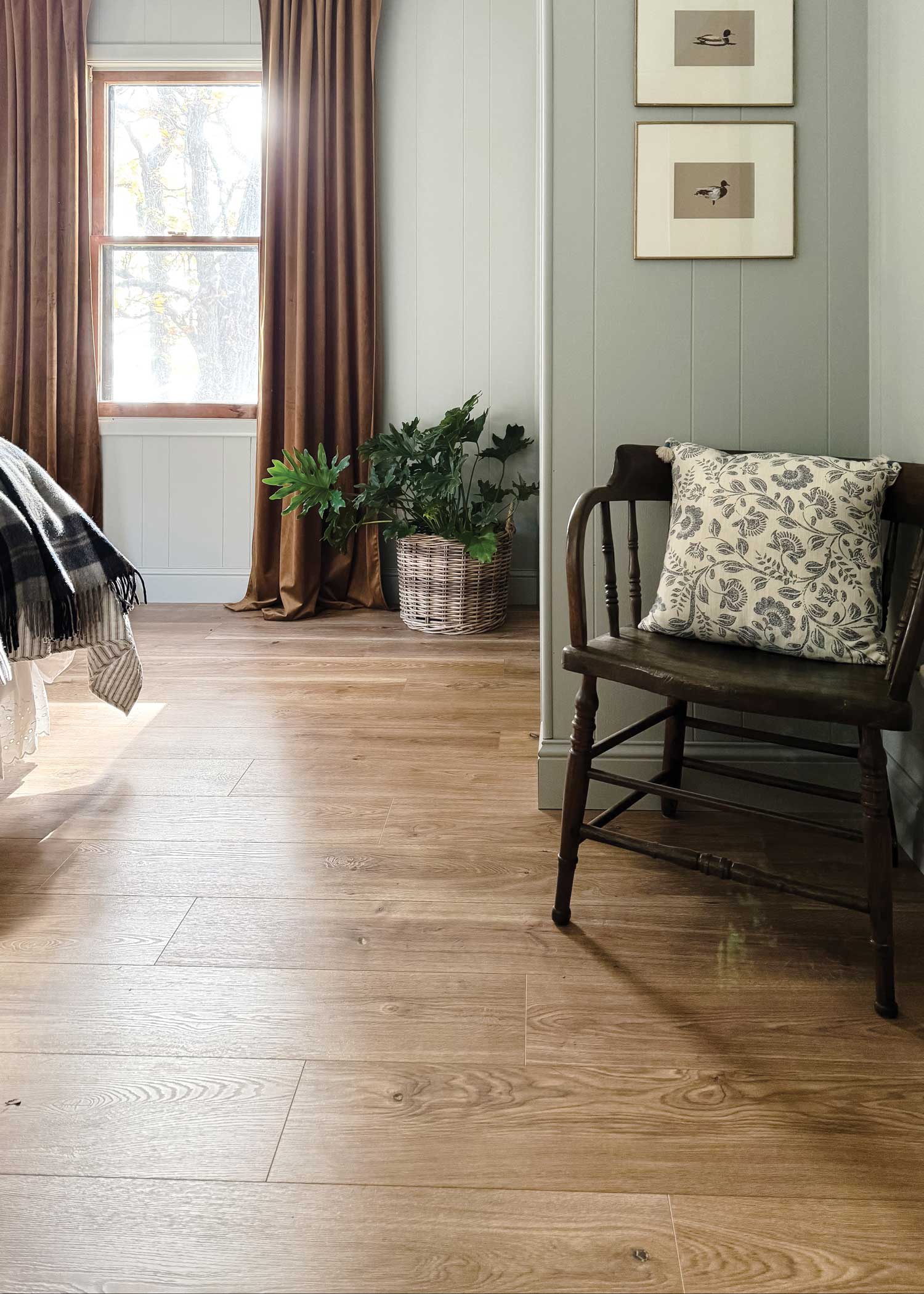duravana bay bridge oak waterproof hybrid resilient flooring in bedroom with dark brown spindle chair and brown curtains plus plaid bedding