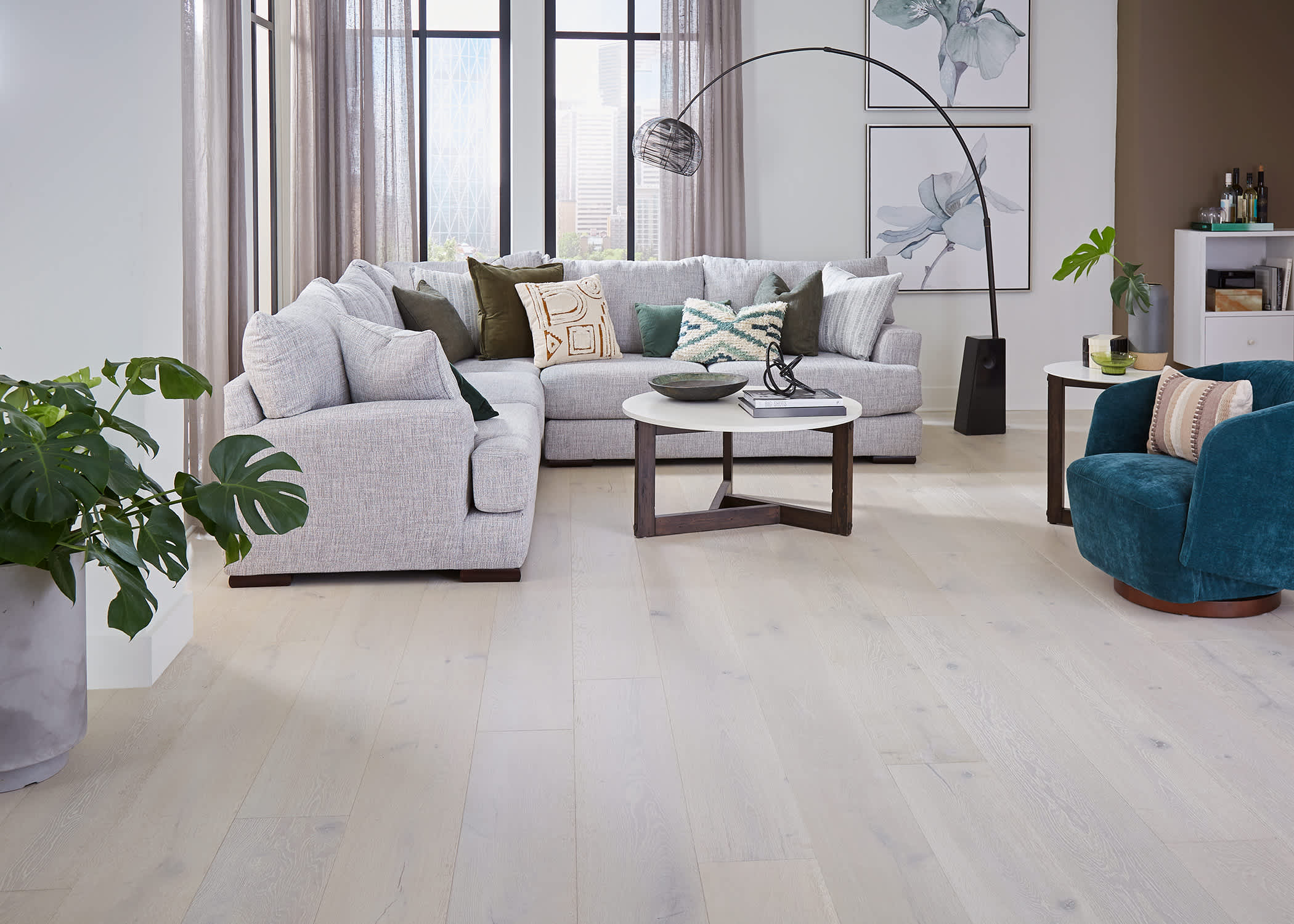 white washed engineered hardwood floor in living room with light gray sectional sofa and dark turquoise barrel side chair and brown walls