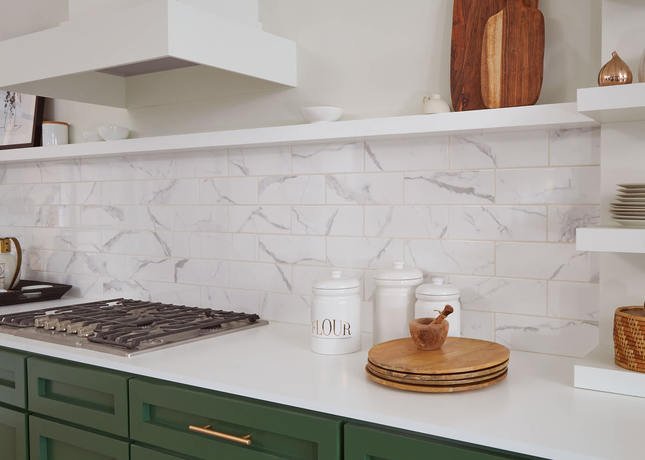 carrara subway tiles in kitchen with green cabinets and floating shelves
