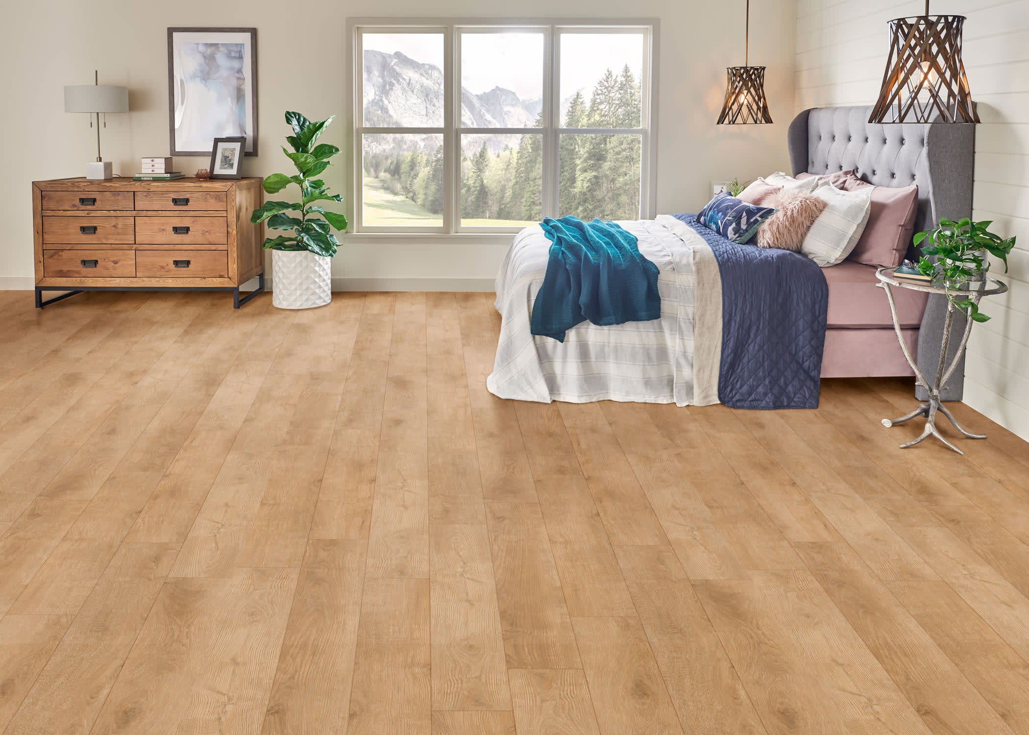blonde waterproof rigid vinyl plank floor in bedroom with gray velvet headboard and pink and turquoise bedding plus wood dresser with large green plant on floor