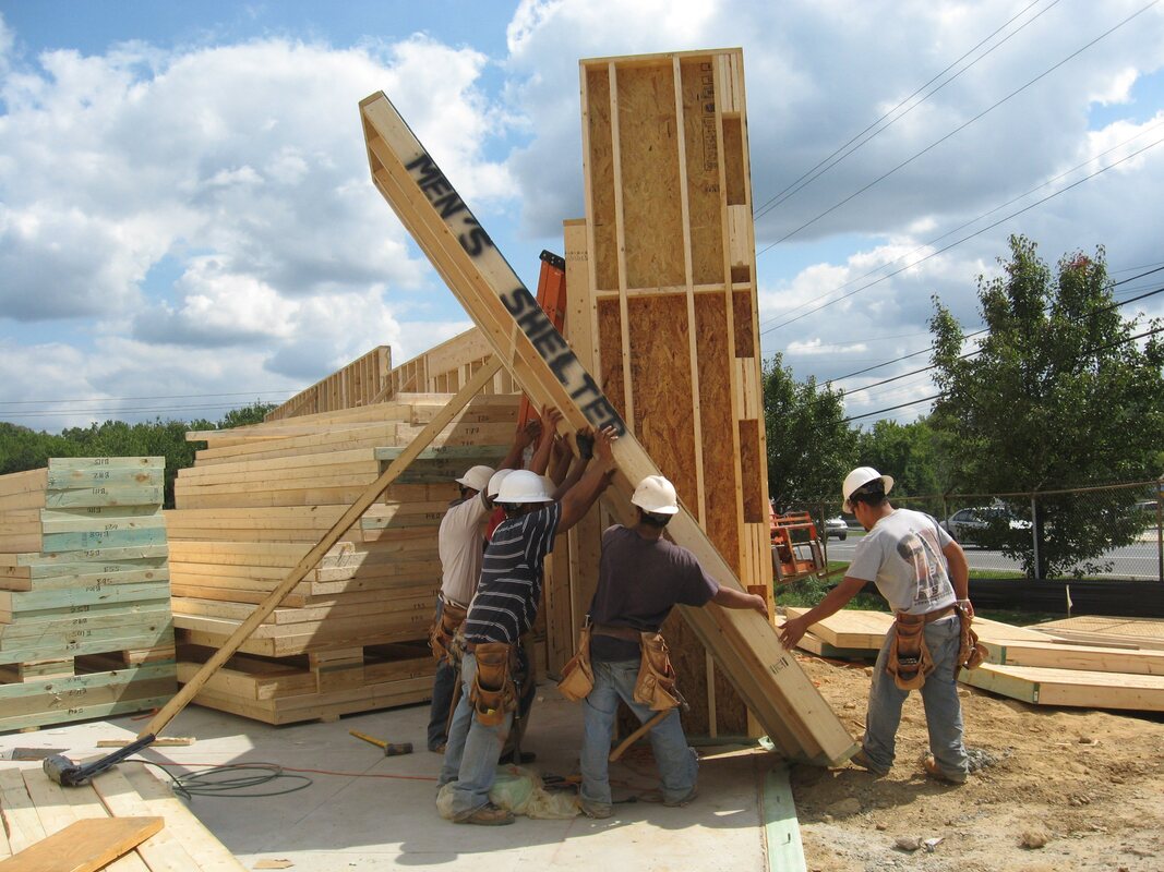 image of builders holding up framing on a construction site for mens shelter