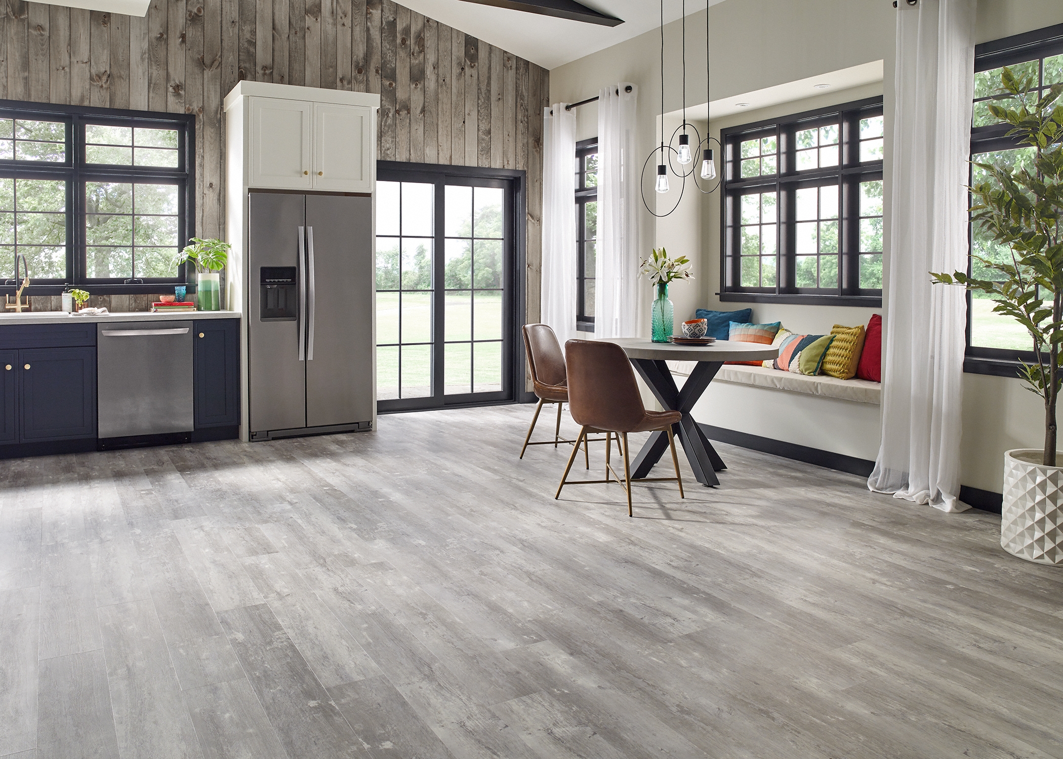 gray rigid vinyl plank in open concept kitchen and dining with blue cabinets plus stainless steel appliances and round dining table with brown dining chairs and bench seating