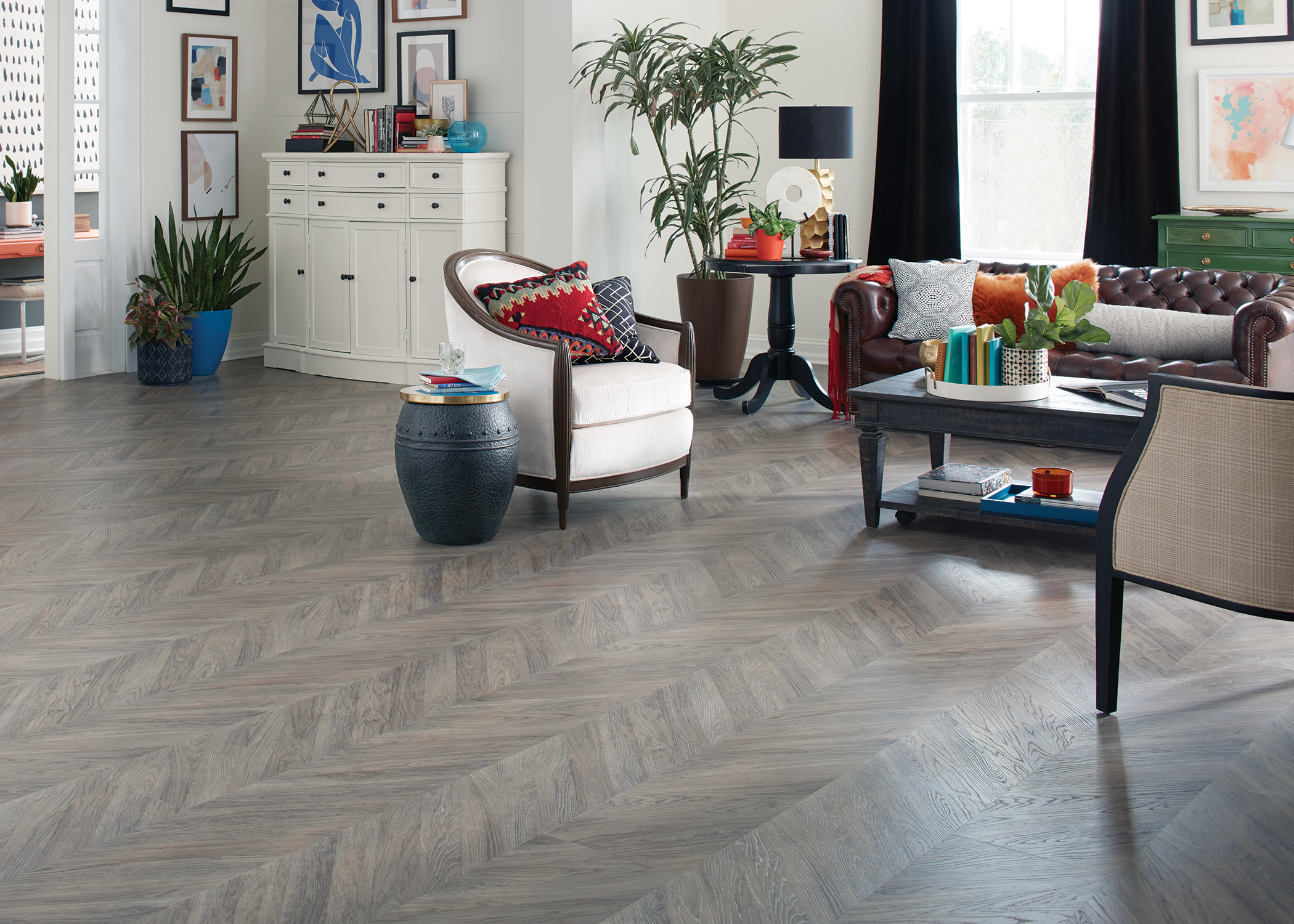 greige chevron waterproof rigid vinyl plank floor in living room with white barrel chair and dark brown leather sofa