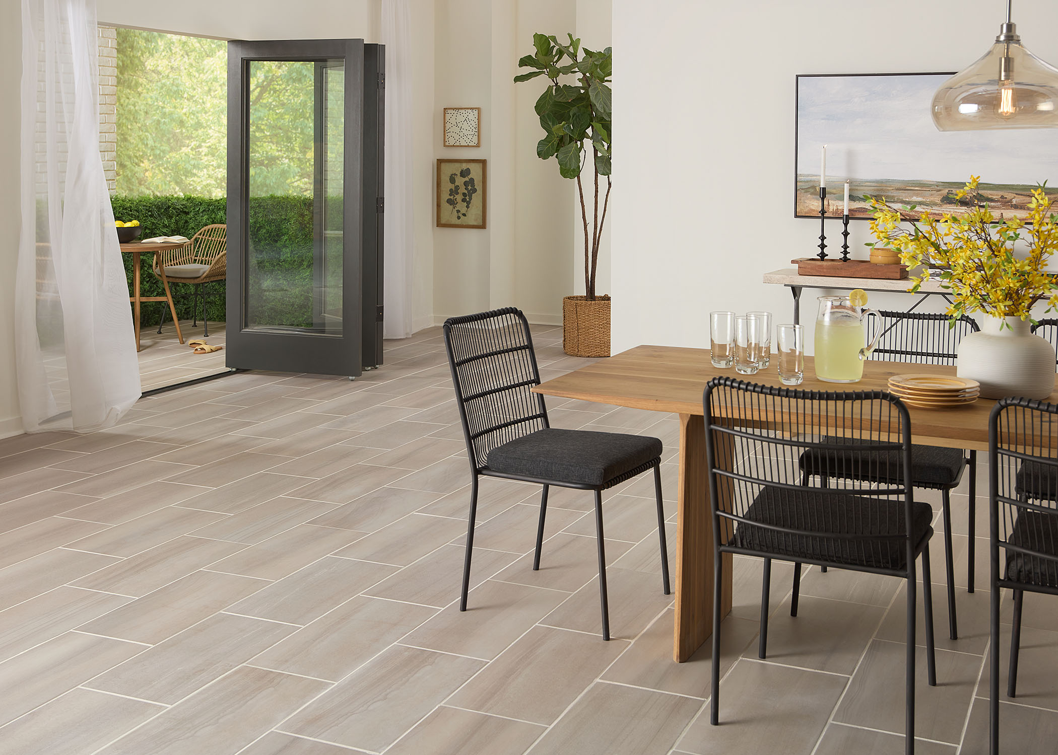 beige waterproof porcelain tile floor in dining room with blonde wood dining table with black metal armless dining chairs and accordion doors open to covered patio with tile on floor