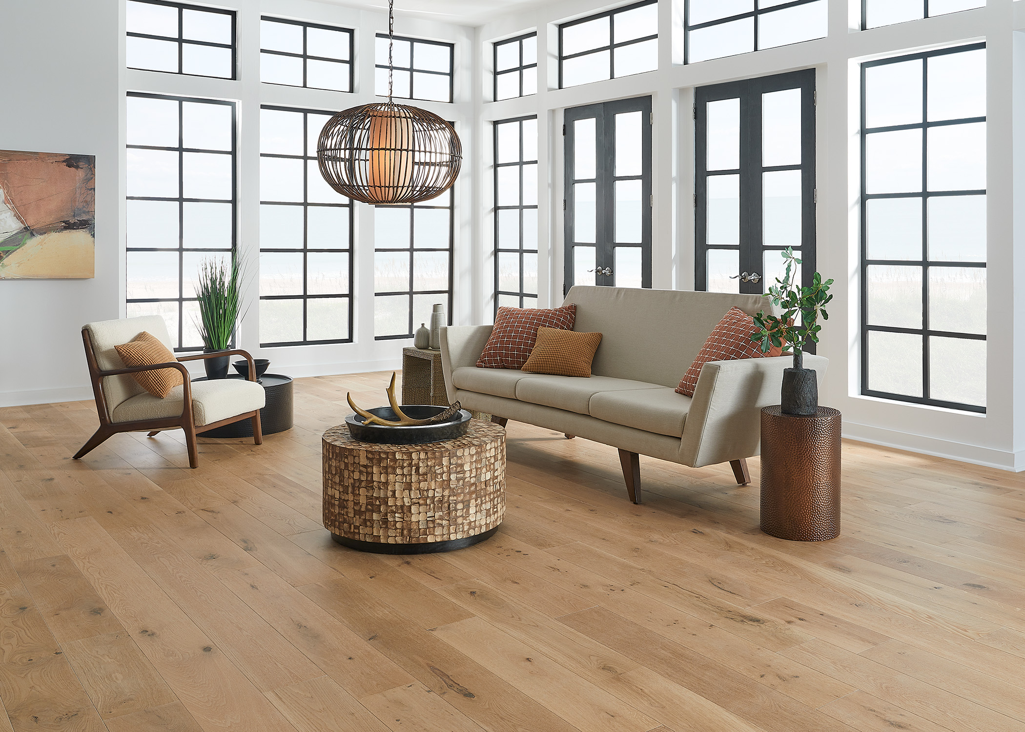 blonde engineered hardwood floor in living room with beige sofa and round wooden coffee table plus rust colored pillows and bronze metal side table