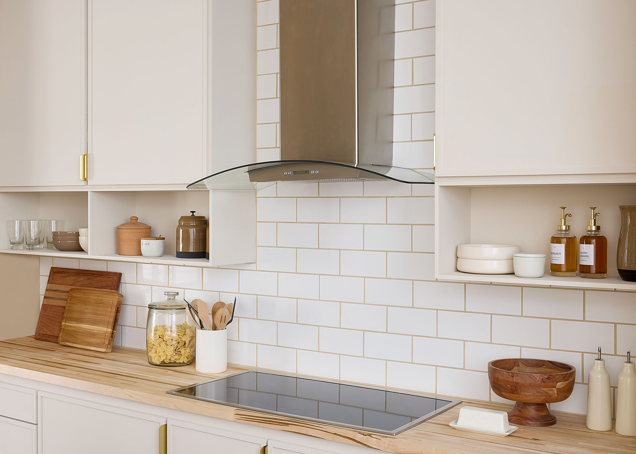white subway tile in kitchen with stainless steel range hood plus glass cooktop and butcher block countertop