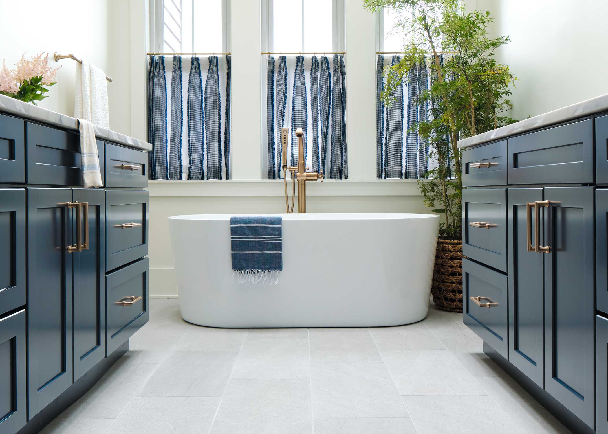 pale silver porcelain tile floor in HGTV Dream Home 2024 bathroom with oval freestanding tub and blue cabinets