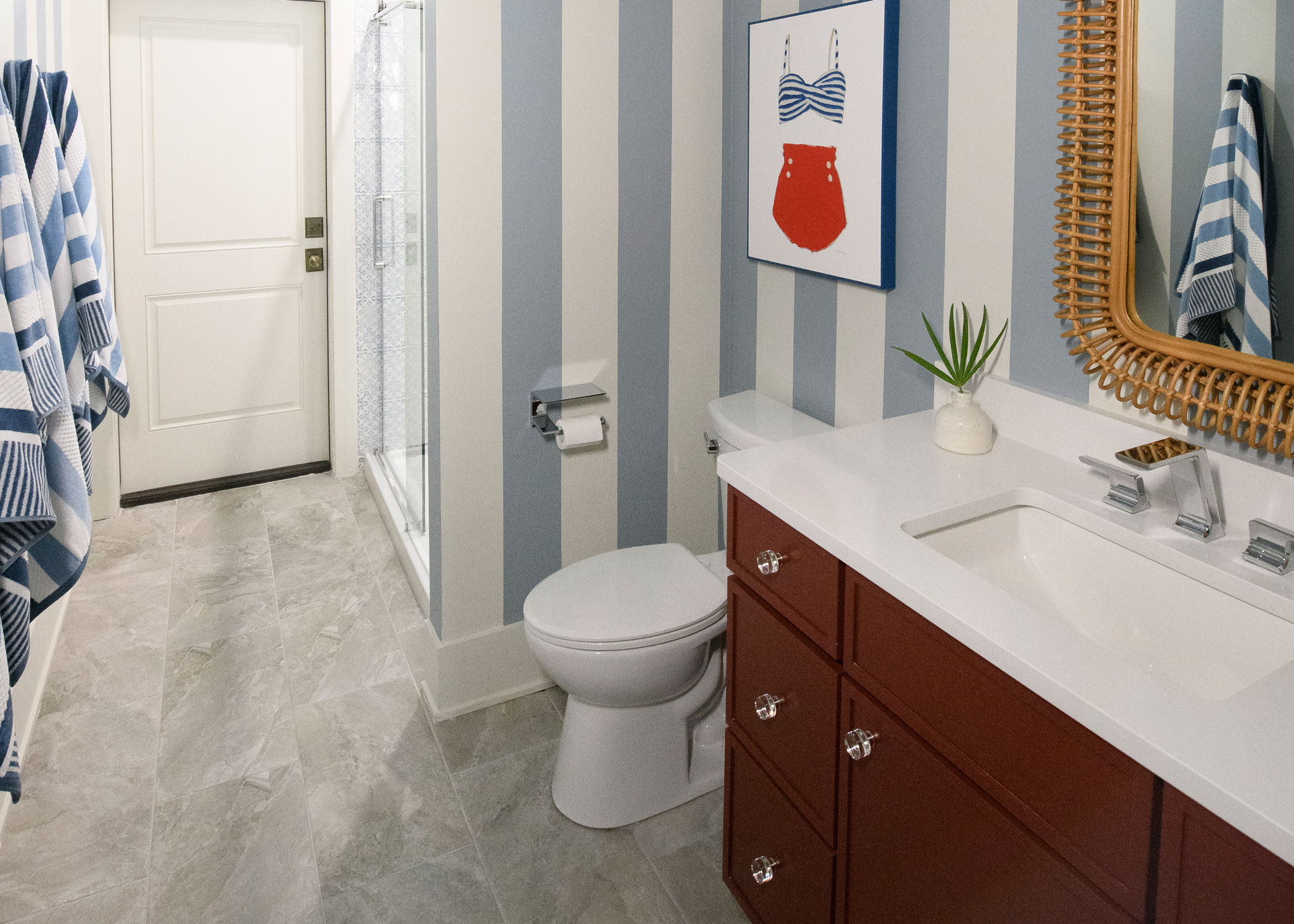 Greige porcelain tile flooring in HGTV Dream Home 2024 bathroom with blue striped wallpaper and dark brown cabinets