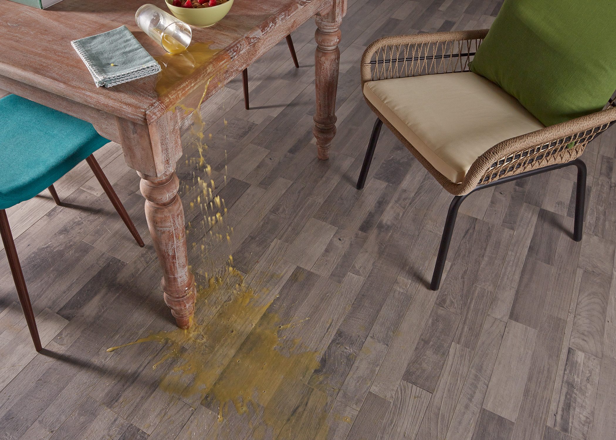 medium brown waterproof laminate floor closeup of floor in front of dining table with rattan dining chair and orange juice spilling from table onto floor