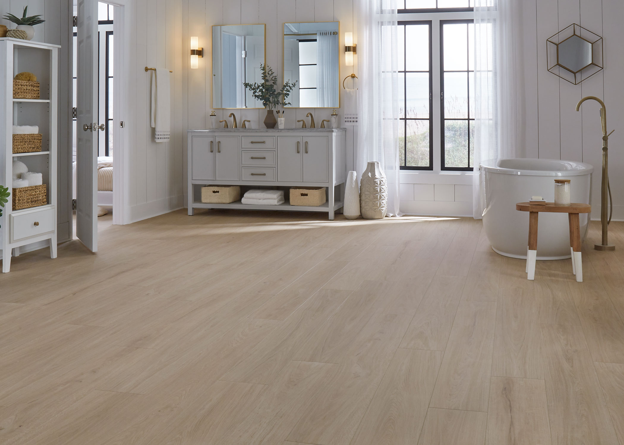 blonde waterproof rigid vinyl plank floor in bathroom with light gray dual vanity plus oval freestanding tub and small light wood stool and shiplap walls