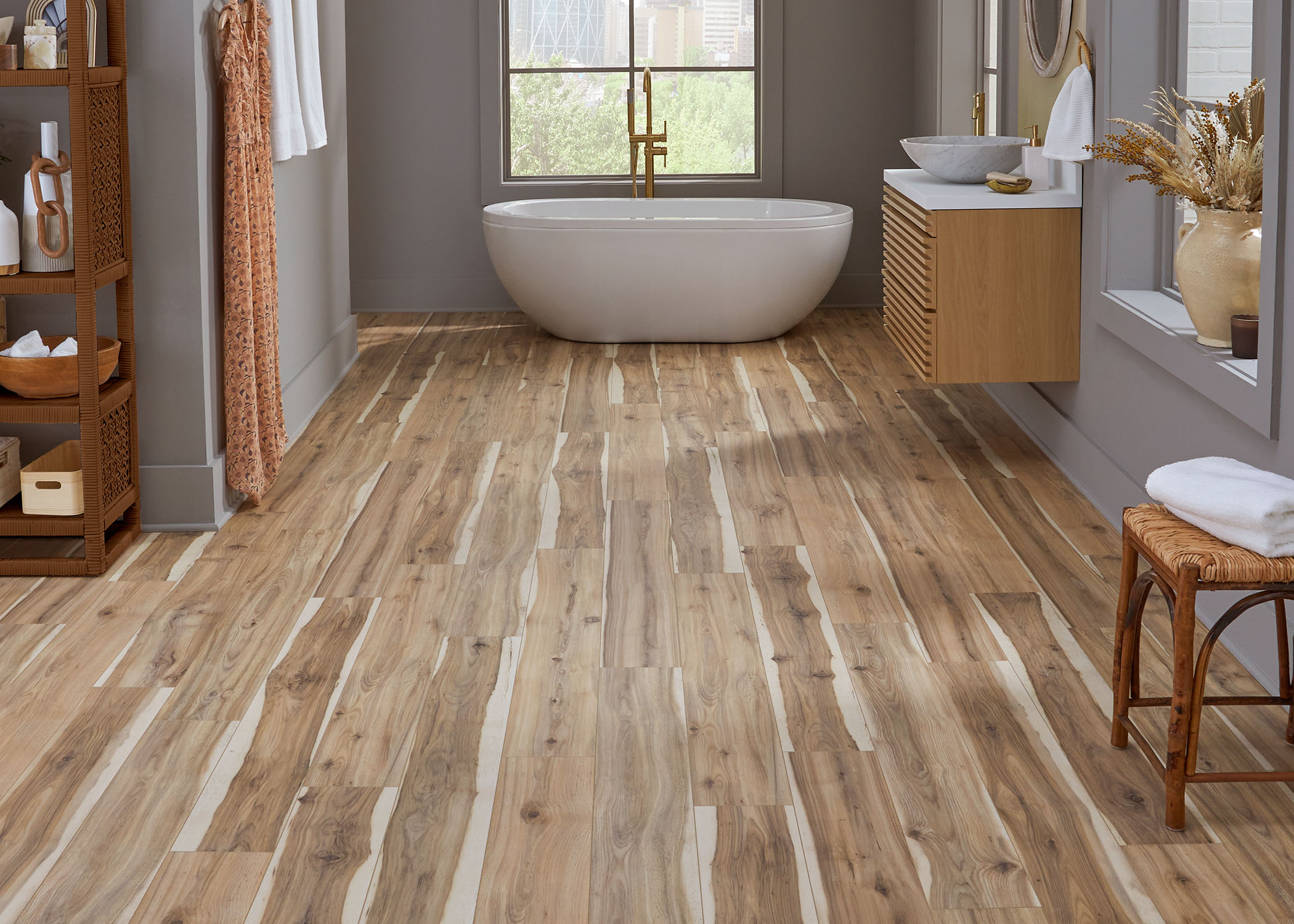 multi tone brown waterproof rigid vinyl plank flooring in bathroom with blonde wood floating vanity plus freestanding oval tub and rattan and cane stool