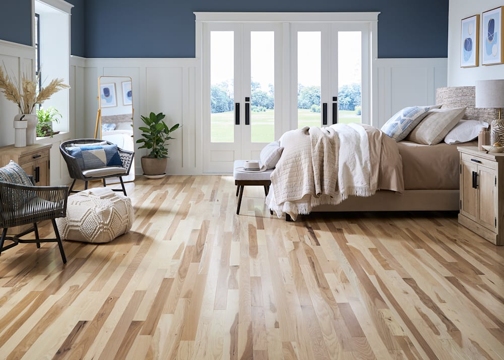 3/4 in. x 3 in. Natural Hickory Solid Hardwood Flooring in bedroom with beige bedding and blue walls