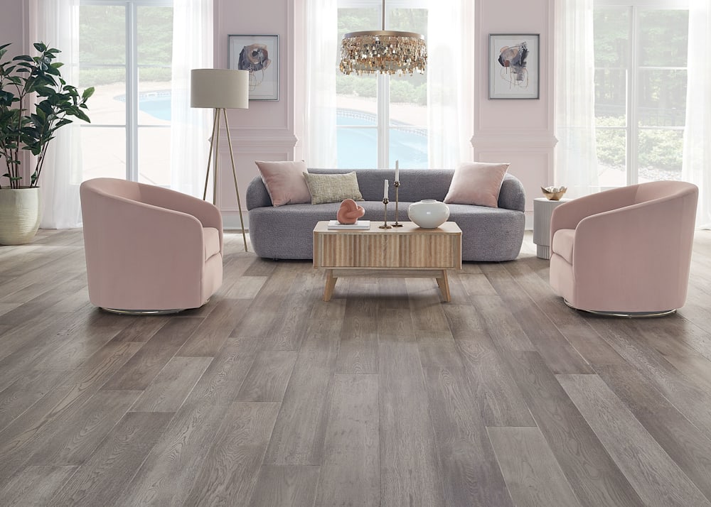 9/16 in. x 7.5 in. Monterey Bay Hickory Engineered Hardwood Flooring in living room with gray sofa with pale pink accent pillows and pink barrel chairs plus blonde wood cocktail table