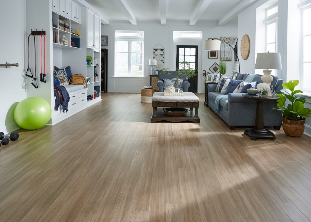 7mm with Pad x 5.11 in Toffee Water-resistant Engineered Bamboo Flooring in living room with dark blue furniture plus white built ins and exercise items on floor