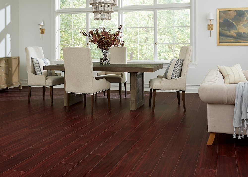 8mm Bloodwood Rigid Vinyl Plank Flooring in dining room with medium brown table plus cream upholstered chairs and dried branches in a vase on the table