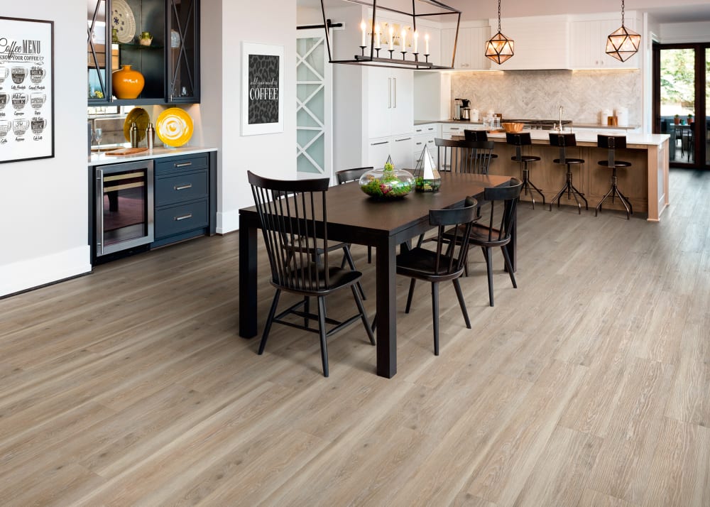 5mm+pad Saint Florent Hickory Rigid Vinyl Plank Flooring in open concept dining room kitchen with dark wood dining table and chairs plus dark blue beverage station plus oversized wood island with chairs