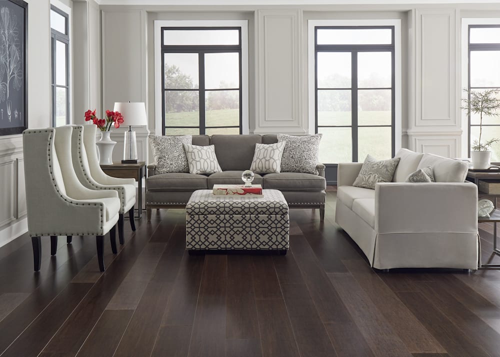 Strand Kona Wide Plank Engineered Click Bamboo Flooring in living room with taupe and beige upholstered furniture plus chain pattern upholstered ottoman and stone colored walls