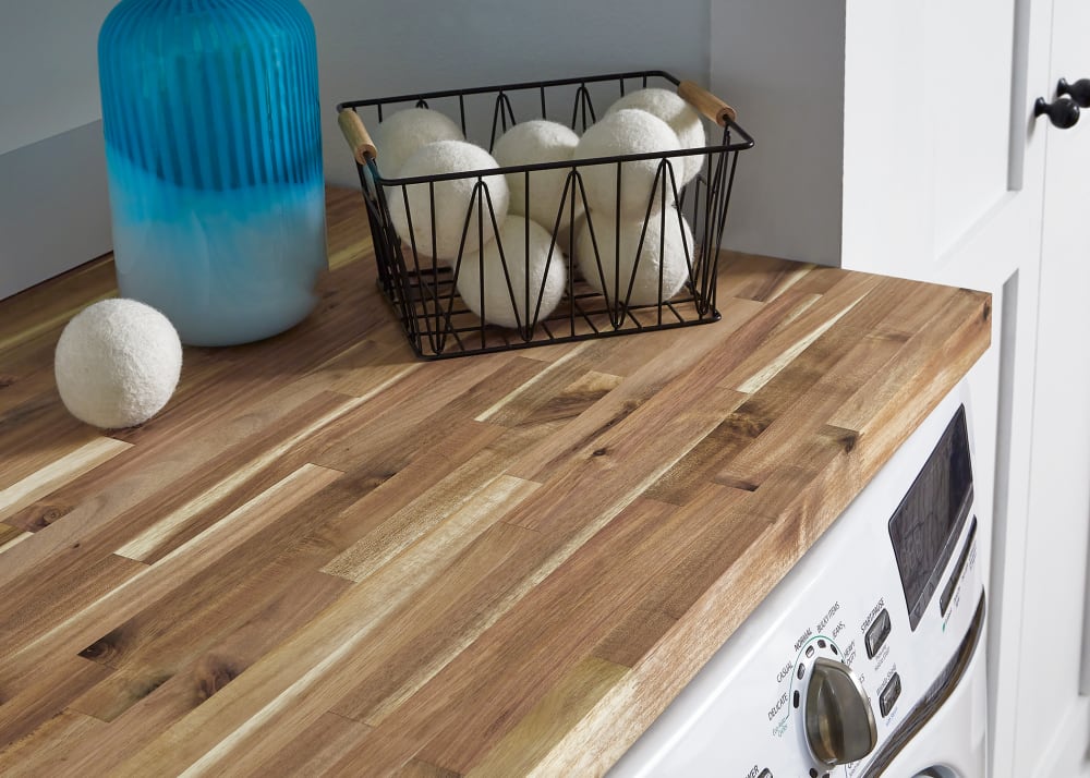 Unfinished Acacia Butcher Block Countertop in laundry room on top of washer and dryer with dryer balls in basket and blue vase