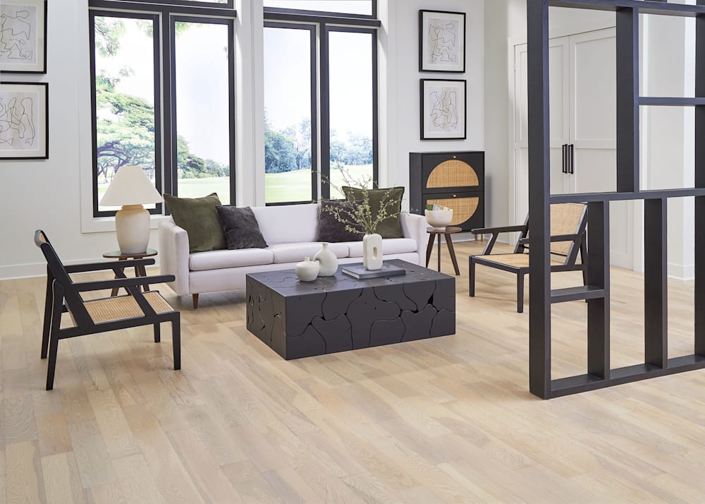 5/16 in. x 5 in. Noland Trail White Oak Quick Click Engineered Hardwood Flooring in living room with japandi styling with beige upholstered sofa plus rattan and black accent chair and black decorative accent wall