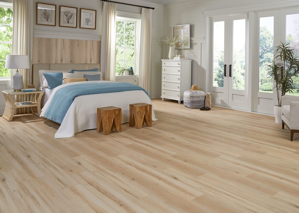 8mm Lake Constance Beech Laminate Flooring in bedroom with white and blue bedding plus flooring on wall behind upholstered headboard and french doors and white dresser