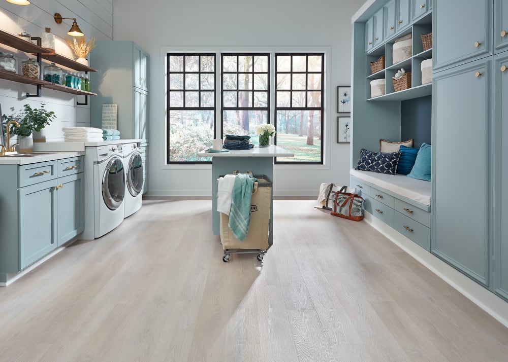 5mm+Pad Helena Grove Oak Rigid Vinyl Plank Flooring in laundry room with pale blue built in cabinets plus small island in center and white washer and dryer plus built in bench with white cushion and blue pillows