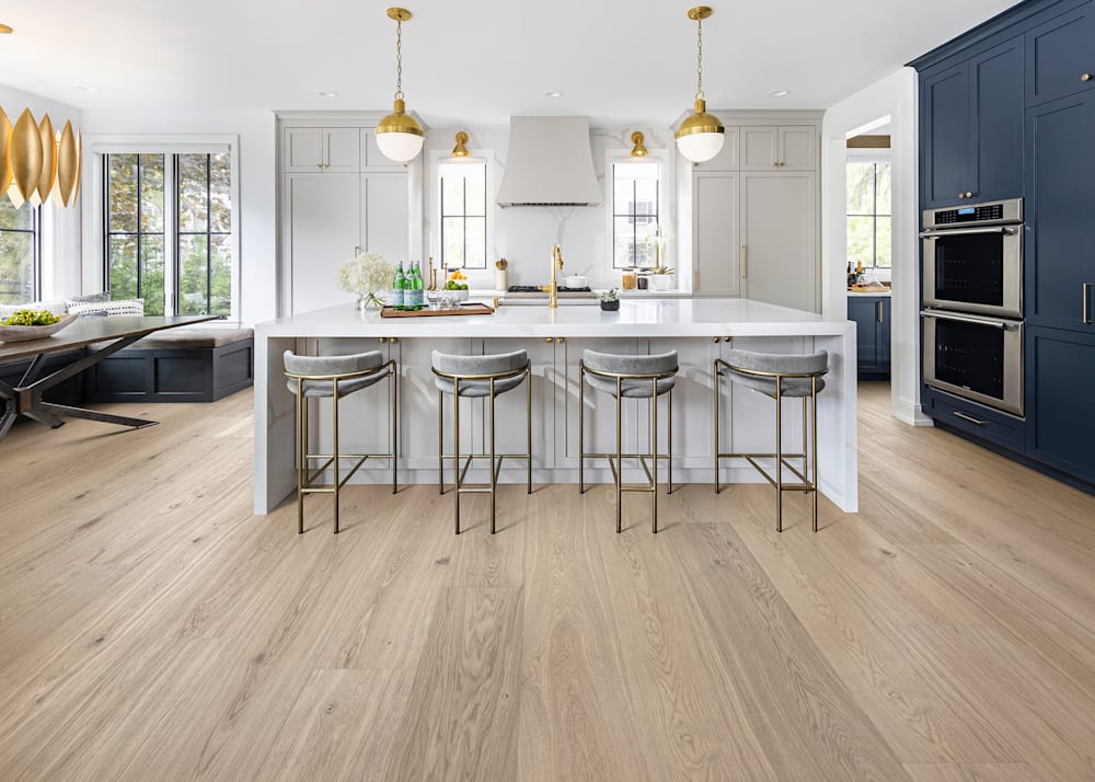 7/16"x10.67" Lagan River White Oak Engineered Hardwood Flooring in kitchen with dark blue floor to ceiling cabinets and oversized White Island with four gray chairs