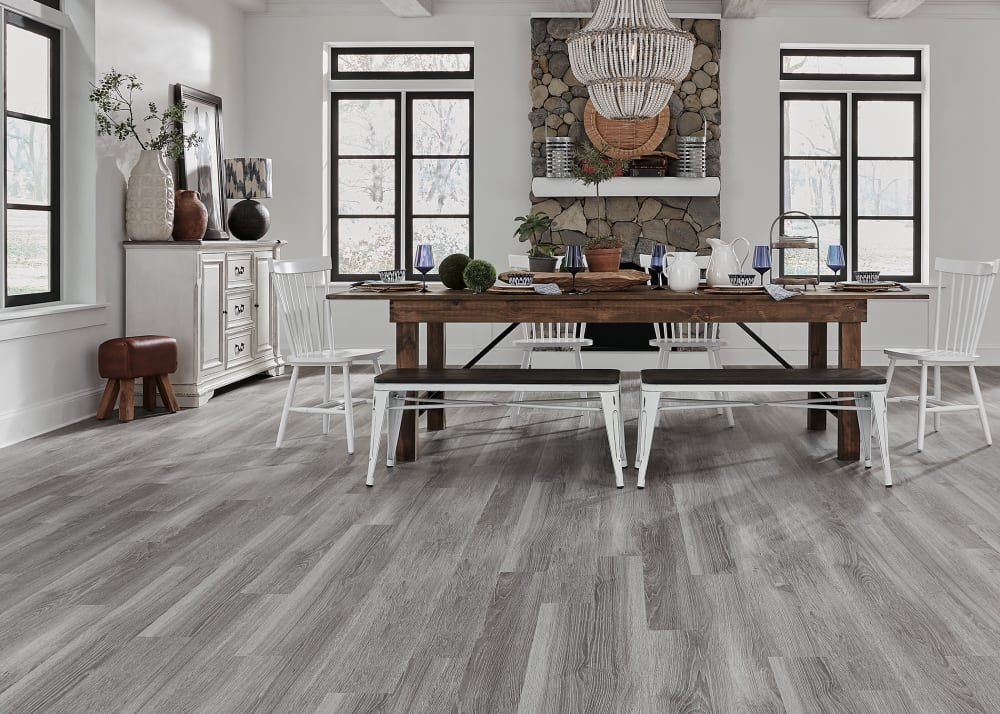 5mm+pad Table Rock Oak Rigid VInyl Plank Flooring in dining room with rustic dark brown dining table plus white distressed bench seats and stone fireplace plus distressed side table with decorative accents
