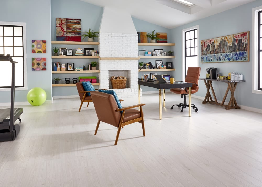 7mm+Pad Urban Mist Oak Hybrid Resilient Flooring in office with light blue walls and white brick fireplace plus black and gold desk and dark brown leather chairs