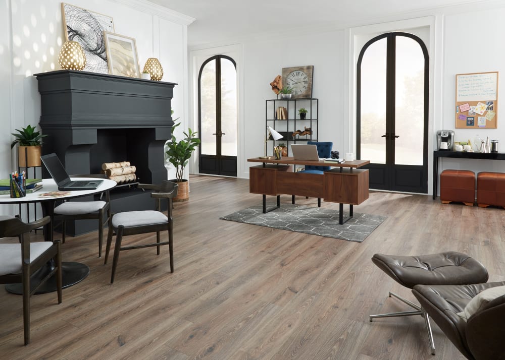 7mm+Pad Sagrada Oak Hybrid Resilient Flooring in office with oversized black fireplace plus dark brown wood desk and small round table with three dark brown and gray chairs