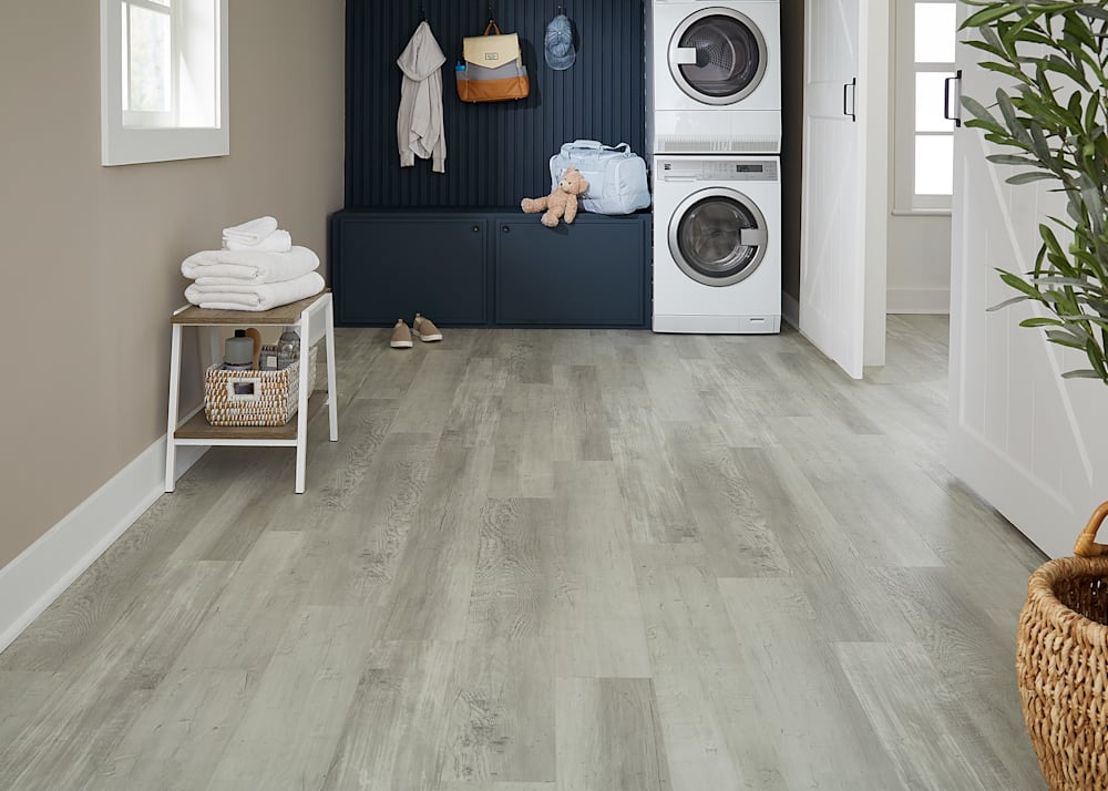 5mm+Pad New Point Coastal Pine Rigid Vinyl Plank Flooring in laundry room with stacked washer and dryer plus dark blue built-ins and small white table with towels and laundry items