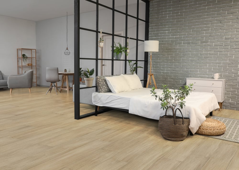 7mm+Pad x 7.48 in Latte Water-resistant Distressed Engineered Bamboo Flooring in studio with white washed brick accent wall and bed with simple bedding