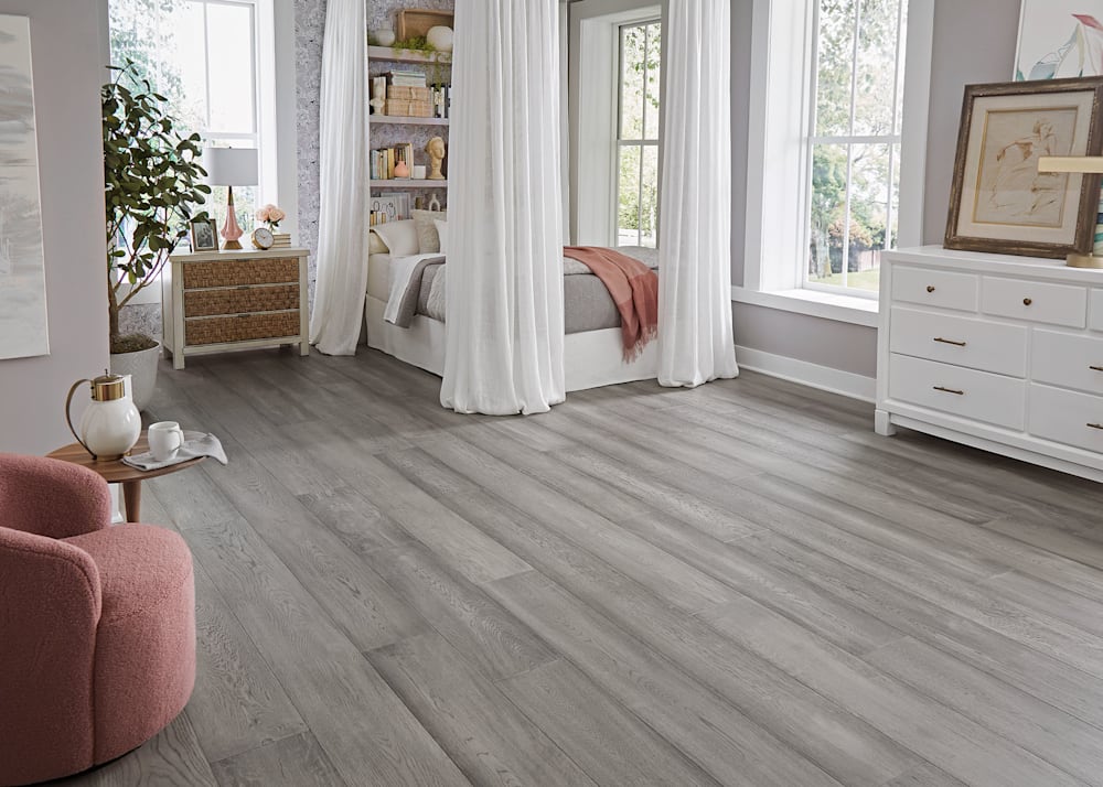 5/8 in x 9.5 in Captiva Beach White Oak Distressed Engineered Hardwood Flooring in bedroom with gray bedding and drapes from four poster plus blush accent chair with white dresser and gray walls