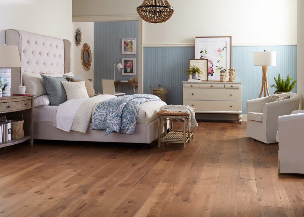 1/2" x 7.4 in Sugar Mill Hickory Distressed Engineered Hardwood Flooring in bedroom with light beige upholstered headboard with blue and cream bedding plus pale blue walls and off white dresser and upholstered accent chairs