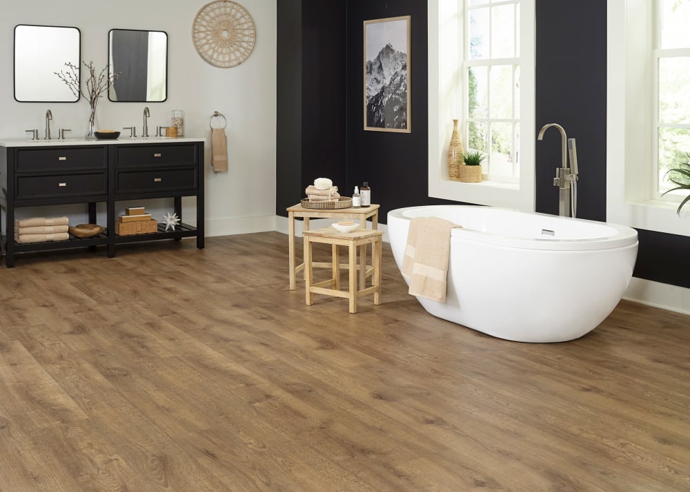 12mm Autumn Cider Oak Waterproof Laminate Flooring in bathroom with black walls plus freestanding oval tub and black dual vanity and light wood stacking tables next to tub