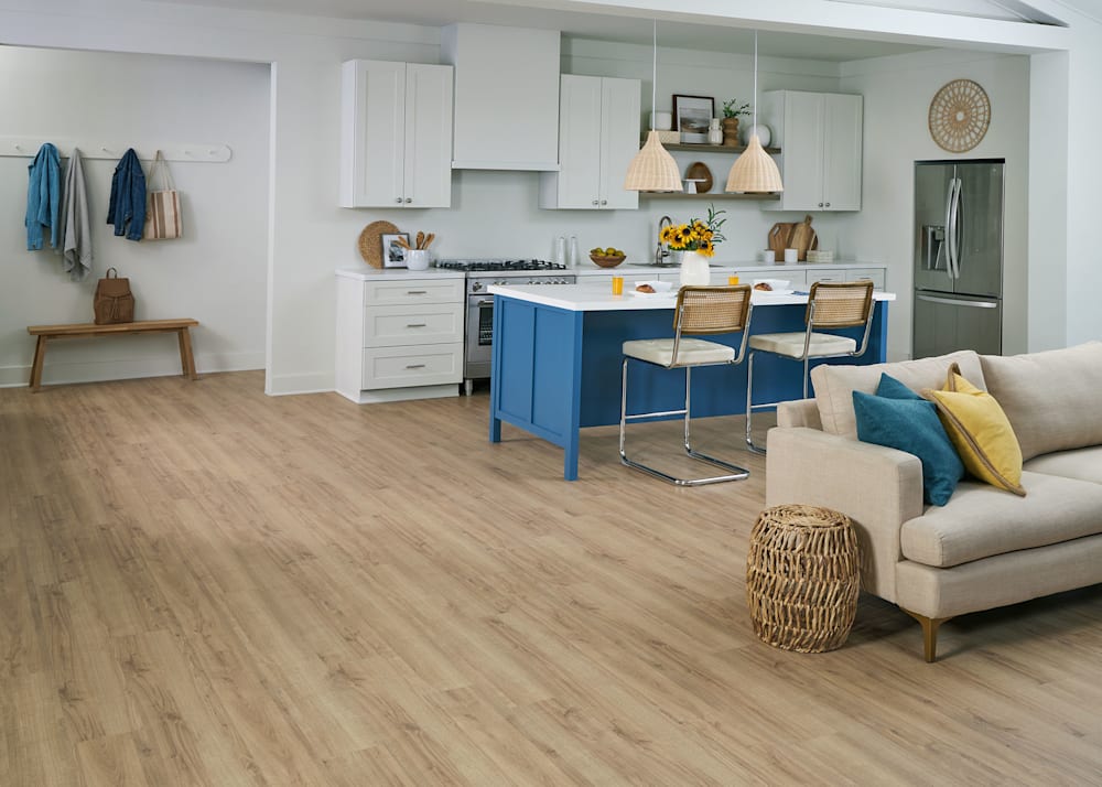 12mm Coastal Oak Waterproof Laminate Flooring in open kitchen and living room with blue island with white cabinets and countertop plus beige sofa with blue and yellow accent pillows