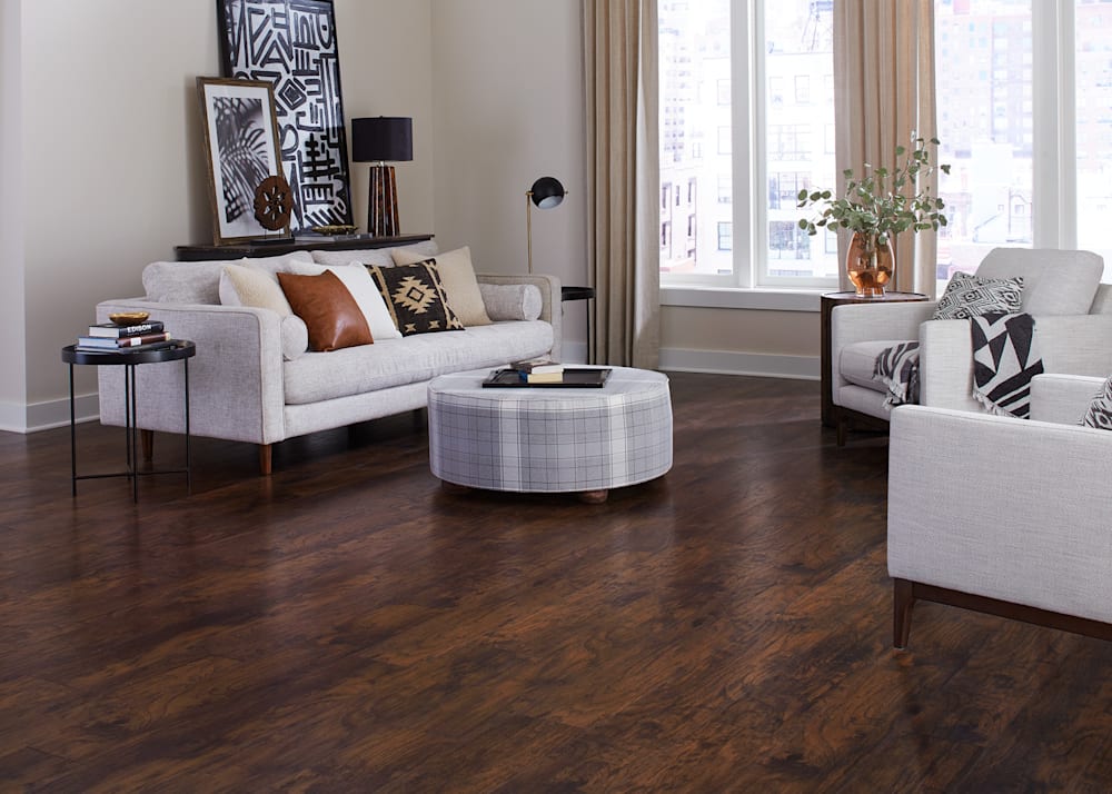 12mm Rustic Realm Hickory Waterproof Laminate Flooring in living room with beige furnishings plus oval ottoman and caramel leather accent pillows