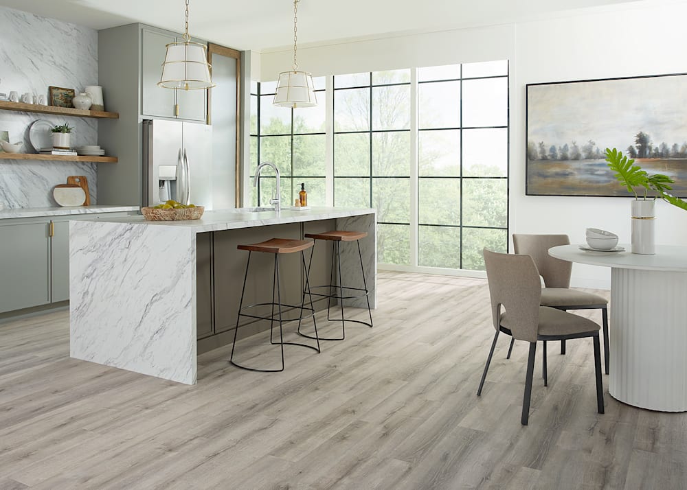 5mm w/Pad Daydream Meadow Oak Rigid Vinyl Plank Flooring in kitchen with oversized waterfall marble island plus gray cabinets and round white dining table and beige upholstered dining chairs