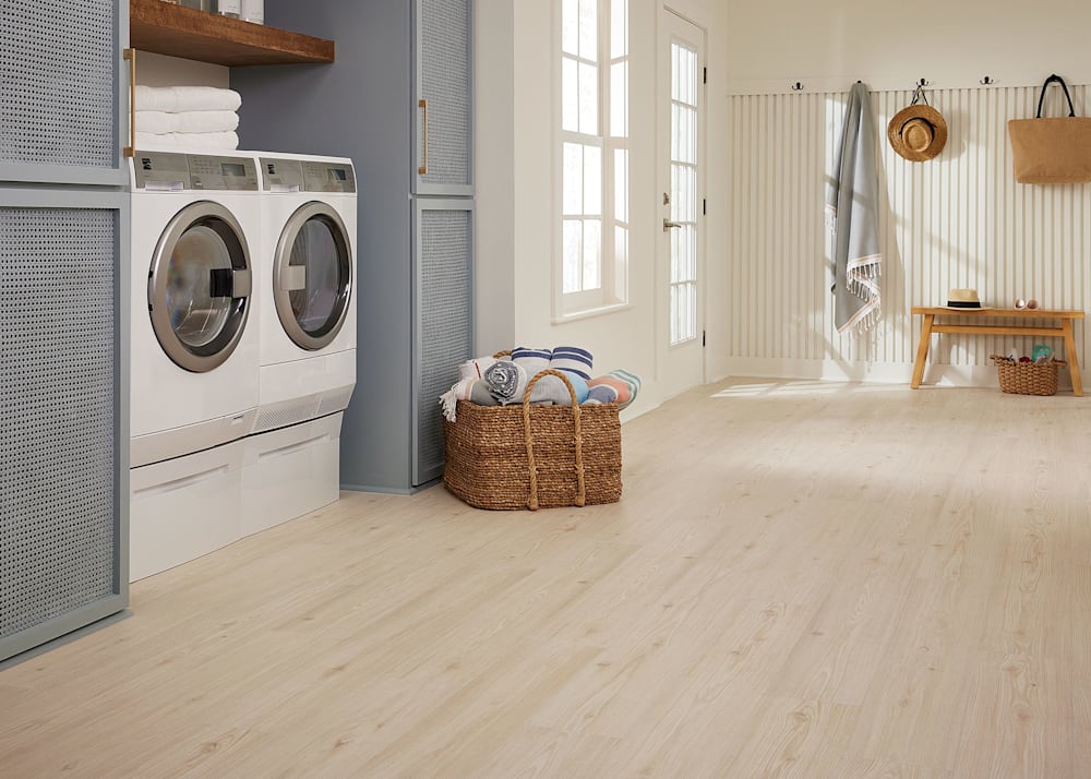 7mm+Pad Voyager Pine Hybrid Resilient Flooring in laundry room with white washer and dryer plus light brown basket with towels and gray cabinets