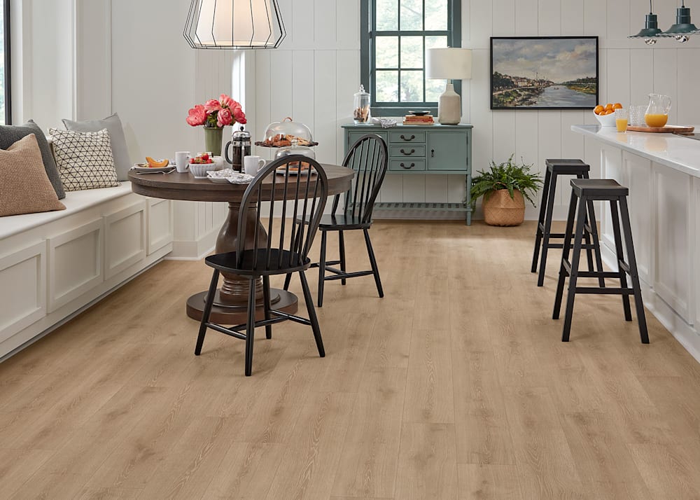 7mm+Pad Lake Lager Oak Hybrid Resilient Flooring in kitchen with down brown round dining table with black dining chairs and bench seating with accent pillows and black bar stools