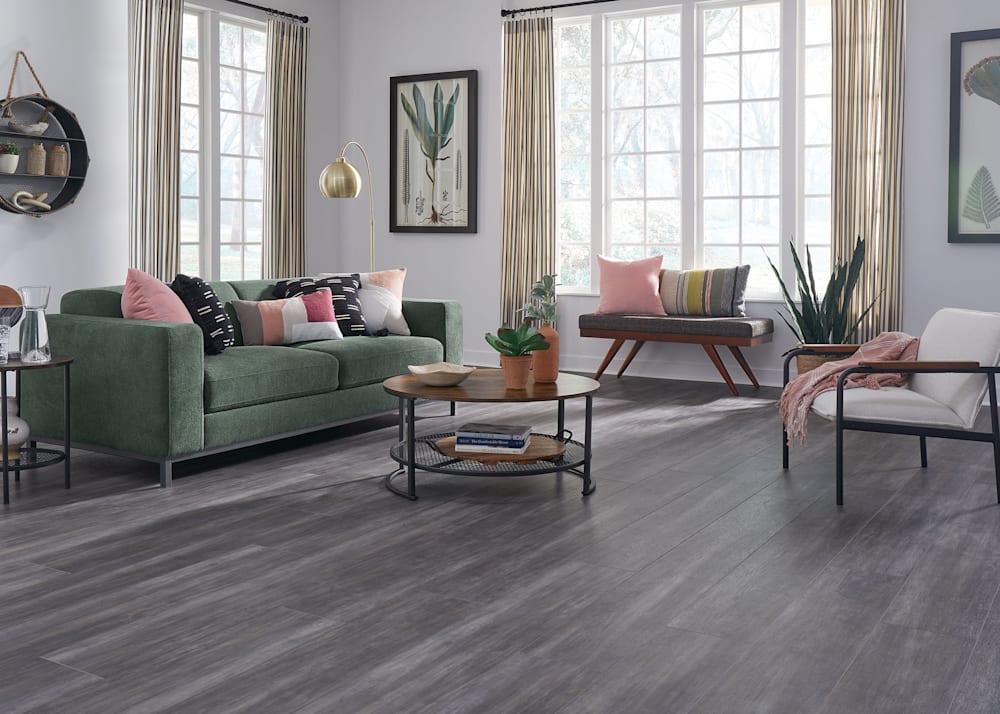 8mm with pad Breckenridge Birch Rigid Vinyl Plank Flooring in living room with green sofa plus blush accent pillows and round wood coffee table and dark gray bench