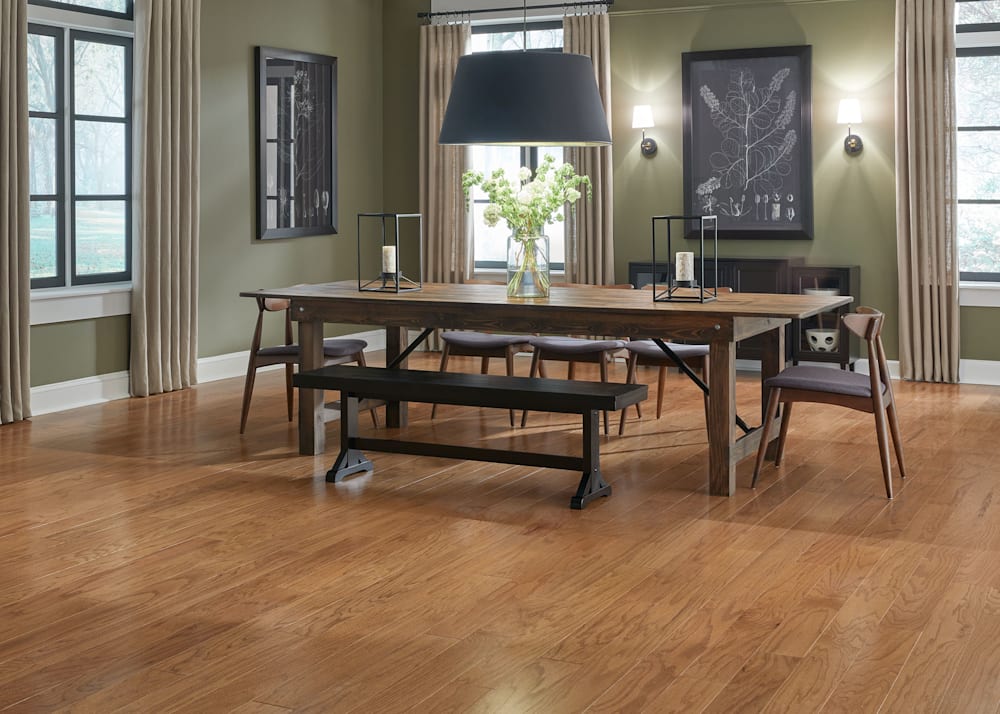 3/8" x 5 in. Butterscotch Oak Engineered Hardwood Flooring in dining room with dark green walls plus medium brown wood dining table and chairs with black drum shade pendant light over table and black and white artwork on walls