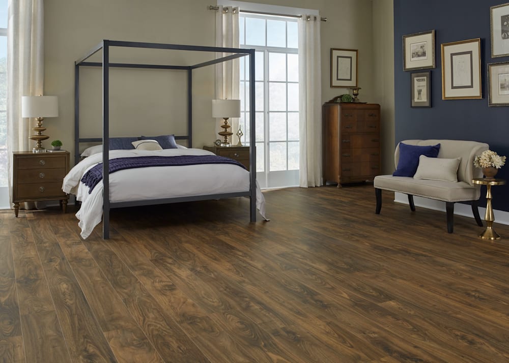 7mm+Pad Rum Cay Walnut Waterproof Hybrid Resilient Flooring in bedroom with four poster bed plus beige settee with gold accent table and dark blue walls