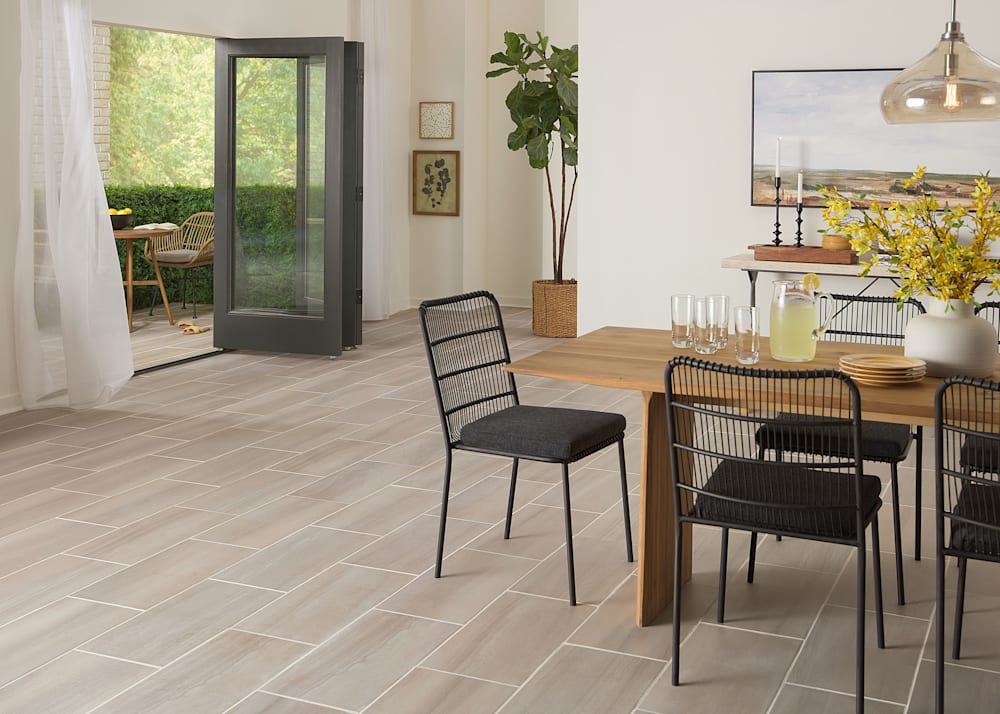 12 in x 24 in Sandstone Earth Porcelain Tile Flooring in dining room with blonde wood dining table with black metal armless dining chairs and accordion doors open to covered patio with tile on floor