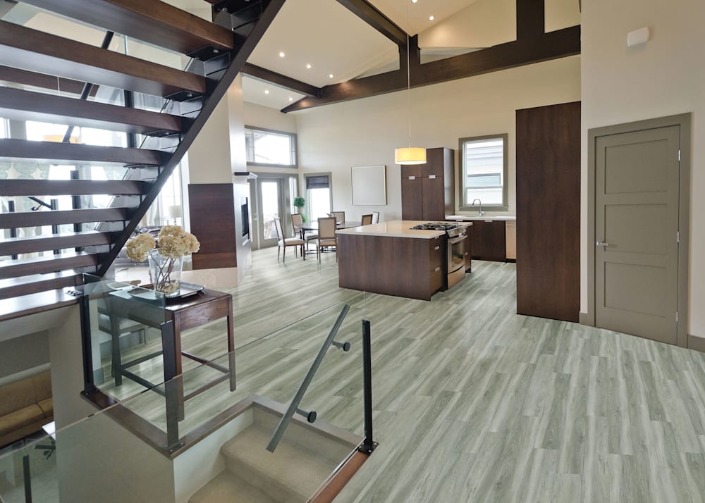 6mm with Pad Cathedral Oak Waterproof Rigid Vinyl Plank Flooring in open concept kitchen and dining with dark brown cabinets plus dark brown floating staircase and taupe colored walls