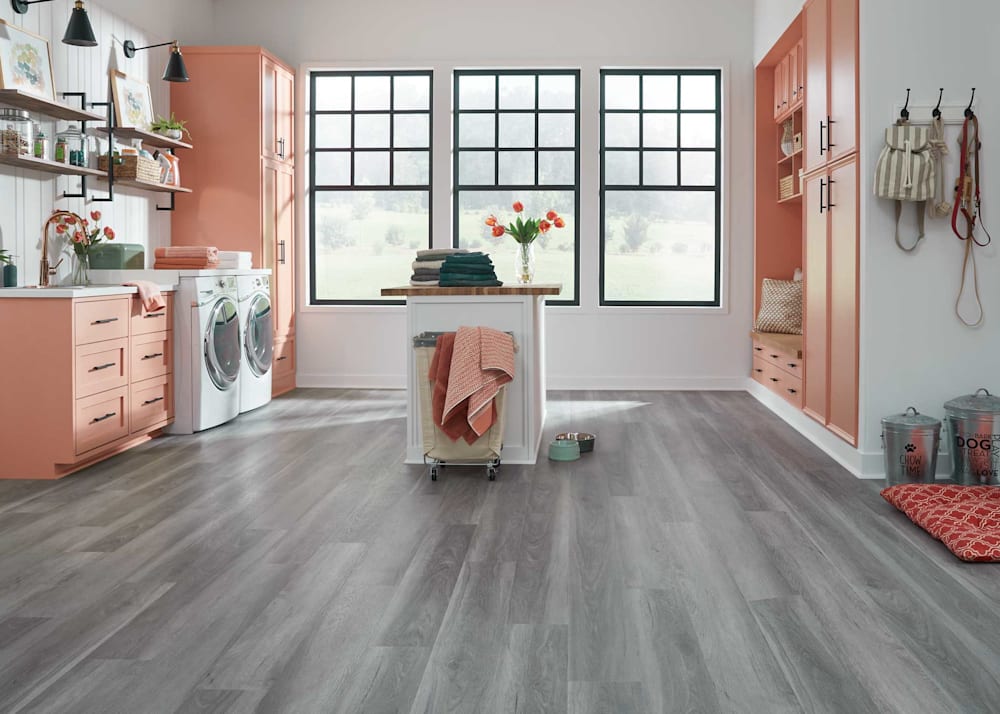 6mm with Pad Cathedral Oak Waterproof Rigid Vinyl Plank Flooring in laundry room with coral cabinets plus white washer and dryer and white island with butcher block countertop